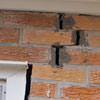A brick wall displaying stair-step cracks and messy tuckpointing on a Henderson home